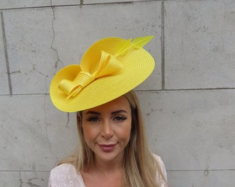 May include: A bright yellow hat with a large bow and a single feather. The hat is made of a straw-like material and has a wide brim.