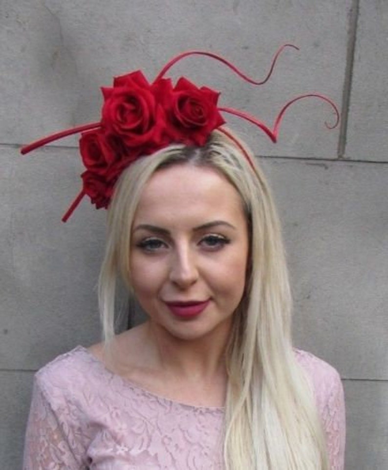 May include: A red flower headband with a cluster of red roses and long, thin, red stems. The headband is worn by a person with long, blonde hair.