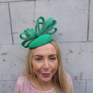 May include: A green fascinator hat with a large bow. The hat is made of a soft, pliable material and has a pleated design.