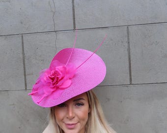 May include: A bright pink wide-brimmed hat with a large pink flower accent. The hat is made of a straw-like material and has a slight curve to the brim.
