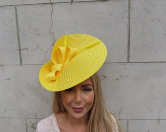 May include: A bright yellow, wide-brimmed hat with a large bow on the side. The hat is made of straw and has a slightly curved brim.