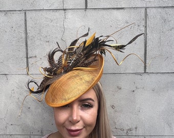 May include: A gold fascinator with brown feathers and gold wire accents. The fascinator is worn on a person's head.
