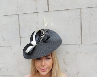 May include: A black and white hat with a large brim and a white bow. The hat is decorated with a small white feather.