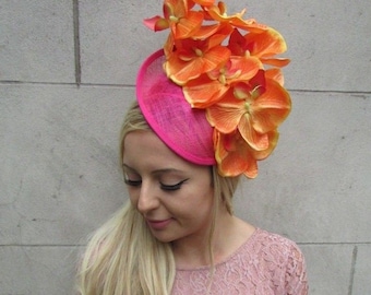 Könnte beinhalten: Ein rosa-oranger Fascinator mit einem großen Strauß aus orangefarbenen Seidenblumen. Der Fascinator ist aus feinem Netzmaterial gefertigt.