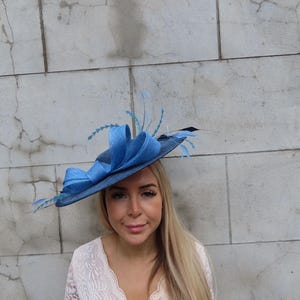 May include: A blue hat with a wide brim and decorative feathers. The hat features a large bow and is made of a woven material. The hat is a stylish accessory for special occasions.