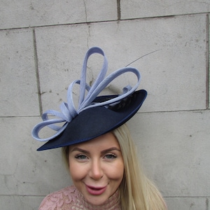 May include: A navy blue hat with a large, light blue ribbon bow. The hat is tilted on the head of a person with long blonde hair.