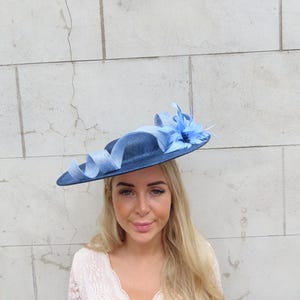 May include: A navy blue hat with a wide brim, adorned with a light blue ribbon and a matching flower. The hat is a stylish accessory, perfect for special occasions. The hat's brim is approximately 14 inches in diameter.