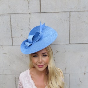 May include: A light blue hat with a large bow on the side. The hat is made of straw and has a wide brim.