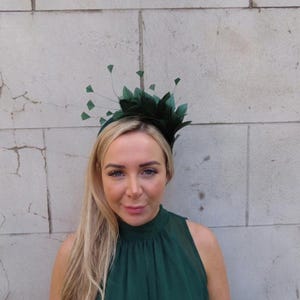 Peut inclure: Un bibi vert foncé composé d'un groupe de plumes vert foncé et de tiges fines semblables à des fils s'étendant vers l'extérieur. L'accessoire est fixé sur un serre-tête fin assorti de couleur vert foncé, formant une parure de tête structurée.