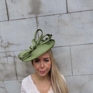 May include: A light green, wide-brimmed hat with a decorative bow. The hat is made of a woven material and has a structured design. The hat is a stylish accessory, suitable for special occasions.