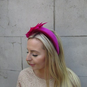 May include: A bright pink velvet headband with a matching pink feather accent. The headband is worn on a person with long blonde hair.