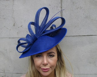May include: A royal blue hat with a wide brim and decorative looped accents. The hat is made of a woven material and features a small, thin feather. The hat is a formal accessory.