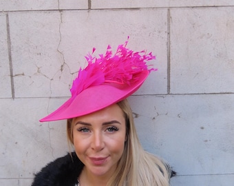 May include: A bright pink hat with a large feather accent. The hat is made of a stiff material and has a wide brim.