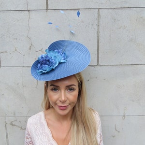 May include: A blue and white hat with a flower accent. The hat is made of straw and has a wide brim. The flower is made of fabric and has a blue and white color scheme.