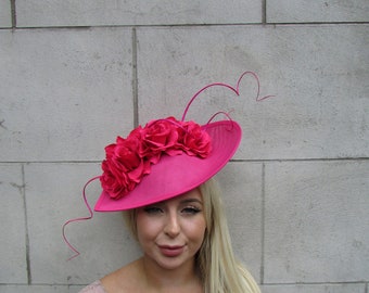 May include: A bright pink hat with a wide brim and a cluster of pink fabric roses on top. The hat has a long, thin, pink feather extending from the side.