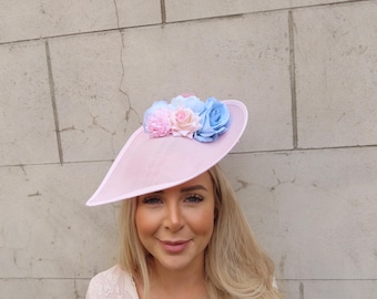 May include: A pink hat with a wide brim and a cluster of pastel pink, blue, and white flowers on top.