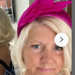 May include: A woman wearing a bright pink headband with feathers. The headband is a wide band with a large feather design on top.