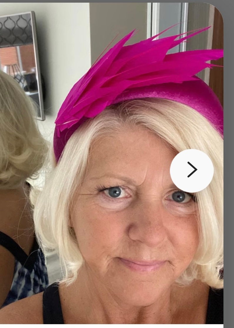 May include: A woman wearing a bright pink headband with feathers. The headband is a wide band with a large feather design on top.