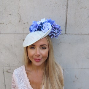 May include: A white hat with a blue and white flower arrangement. The hat is made of a straw-like material and has a wide brim.