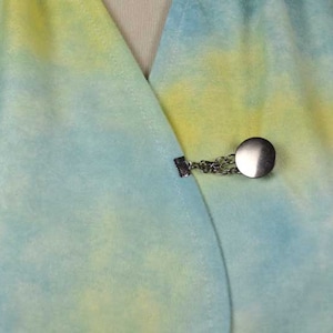 Puede incluir: Primer plano de una tela de teñido anudado de color azul claro y amarillo con un cierre plateado. El cierre es un círculo redondo con una cadena unida.