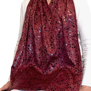 May include: A burgundy bib with a silver and black confetti pattern. The bib is worn by a person sitting in a chair.