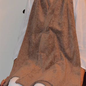 May include: A brown terry cloth bib with a V-neck opening. The bib is worn by a person sitting on a chair.