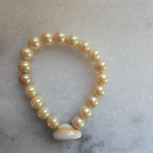 May include: A white pearl bracelet with a shell charm. The bracelet is made of small, round pearls and has a simple design.