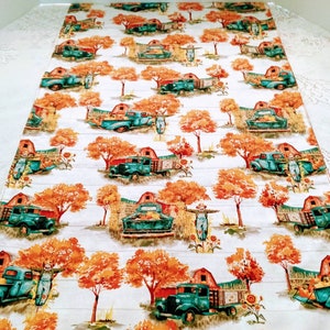 Può includere: Runner da tavolo bianco con un motivo ripetuto di camion turchese, alberi arancioni, fienili rossi e spaventapasseri. Il design evoca il tema del raccolto autunnale, con un'estetica rustica e vintage.