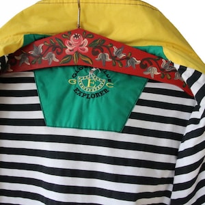 May include: A yellow, green, and black striped jacket with a zipper closure. The jacket has a green patch on the back with the text "Global Club Explorer" and a logo with a letter "E" inside a shield.