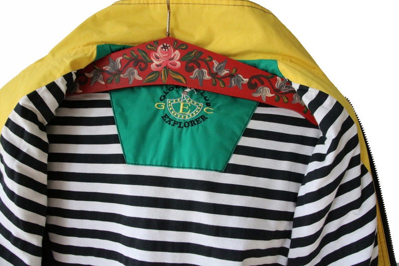 May include: A yellow, green, and black striped jacket with a zipper closure. The jacket has a green patch on the back with the text "Global Club Explorer" and a logo with a letter "E" inside a shield.