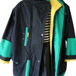 May include: A black, green, and yellow hooded jacket with a zipper closure. The jacket has a large pocket on the front and a contrasting green and yellow trim.