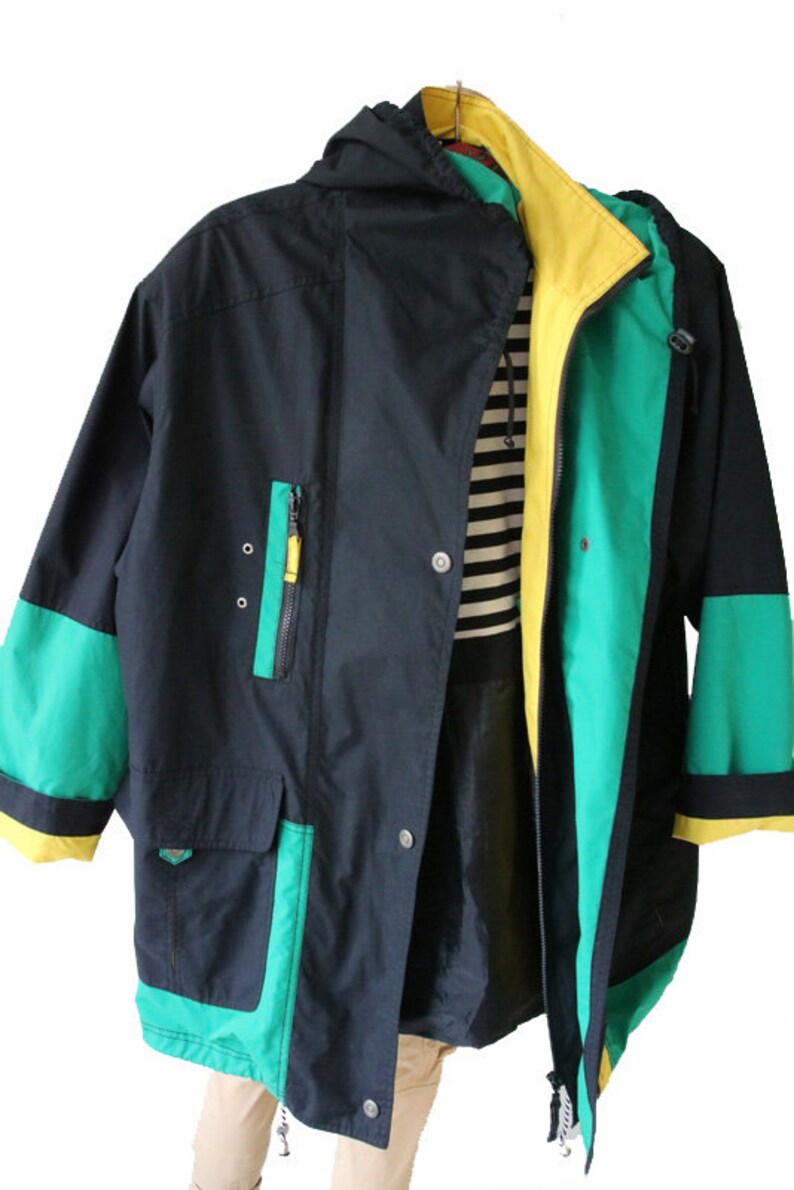 May include: A black, green, and yellow hooded jacket with a zipper closure. The jacket has a large pocket on the front and a contrasting green and yellow trim.