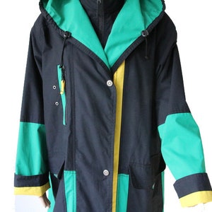 May include: A black hooded jacket with green and yellow accents. The jacket has a zipper closure and a button closure. The hood has a drawstring.