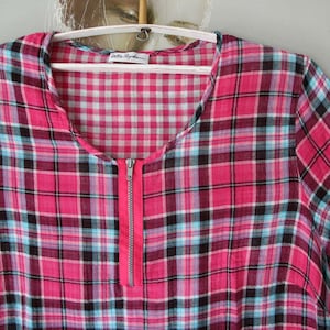 Könnte beinhalten: Ein pinkfarbenes und schwarzes kariertes Hemd mit einem Reißverschluss an der Vorderseite. Das Hemd hat ein Gingham-Muster an der Innenseite des Kragens.