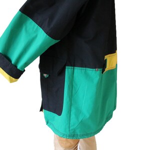 May include: A black, green, and yellow jacket with a zipper closure and a large pocket on the front. The jacket has a contrasting color design with a green and yellow panel on the bottom.