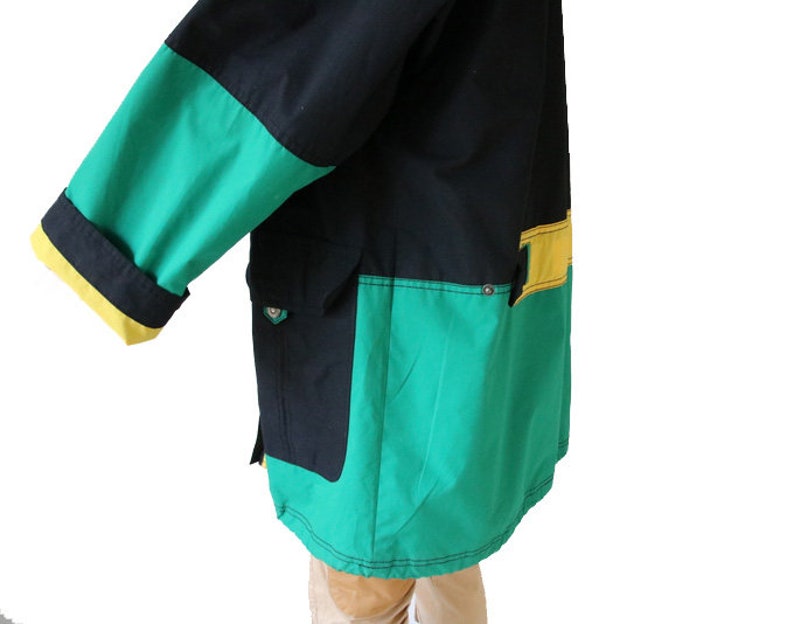 May include: A black, green, and yellow jacket with a zipper closure and a large pocket on the front. The jacket has a contrasting color design with a green and yellow panel on the bottom.