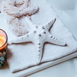 May include: A white ceramic starfish on a white towel with a lit candle in a glass jar.