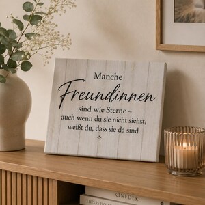 Könnte beinhalten: Ein rechteckiges weißes Holzschild mit vertikaler Bretteroptik und schwarzem Aufdruck: Manche Freundinnen sind wie Sterne – auch wenn du sie nicht siehst, weißt du, dass sie da sind, ergänzt durch ein kleines Sternsymbol.