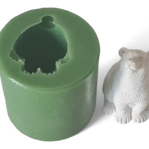 May include: Green silicone mould for making a small polar bear figurine. The mould is cylindrical with a hollow interior shaped like a polar bear. A white polar bear figurine is shown next to the mould.