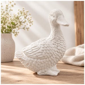 Könnte beinhalten: Eine weiße Entenfigur mit detailliert geformten Federn am ganzen Körper, einem glatten Schnabel und definierten Augen. Die Ente ist in stehender Position dargestellt, wobei der Kopf leicht zur Seite gedreht ist und eine strukturierte Oberfläche zeigt.
