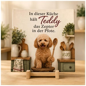 Op de afbeelding: Een vierkant decoratief bord met een lichtbruine hond met krullend haar die op een klein krukje zit en een houten lepel vasthoudt. De tekst luidt: In dieser Küche hält Teddy das Zepter in der Pfote. De achtergrond toont een keuken.