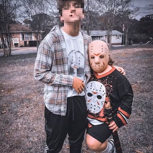 May include: Two people wearing Halloween costumes. One person is wearing a plaid shirt and black pants. The other person is wearing a black and red hockey jersey with a white hockey mask.