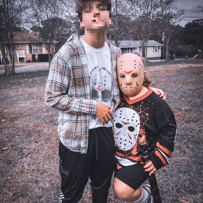 May include: Two people wearing Halloween costumes. One person is wearing a plaid shirt and black pants. The other person is wearing a black and red hockey jersey with a white hockey mask.