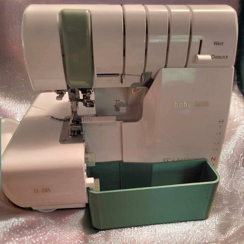 May include: A white Baby Lock EF-205 serger with a green accessory tray. The serger has a wave overlock function and a 55th Anniversary logo.