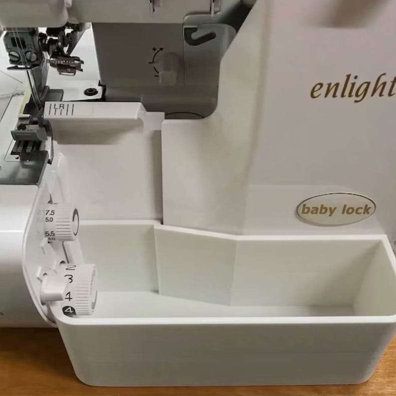 May include: White Baby Lock enlighten serger sewing machine with a white plastic accessory tray. The machine has a dial with numbers 2, 3, and 4. There is another dial with numbers 5.0, 5.5, 6.0, 6.5, and 7.5.