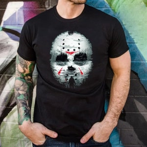 May include: A black t-shirt with a white and red graphic print of a hockey mask with a forest scene in the background.