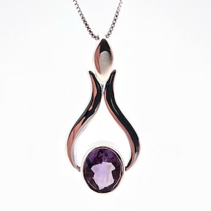 May include: A silver pendant necklace featuring a purple amethyst gemstone. The pendant has a distinctive design with two curved silver pieces forming a teardrop shape.