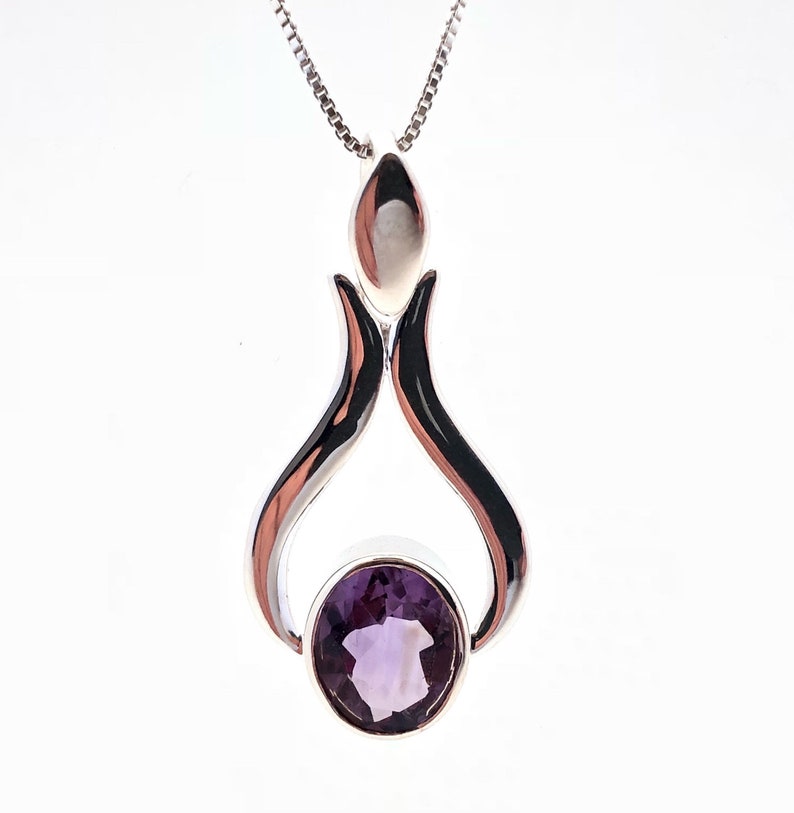 May include: A silver pendant necklace featuring a purple amethyst gemstone. The pendant has a distinctive design with two curved silver pieces forming a teardrop shape.