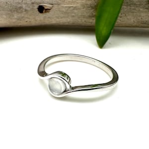 May include: A silver ring with a white moonstone set in a curved band.