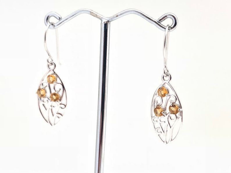 May include: Silver dangle earrings with a leaf design and multiple small, round, yellow gemstones.